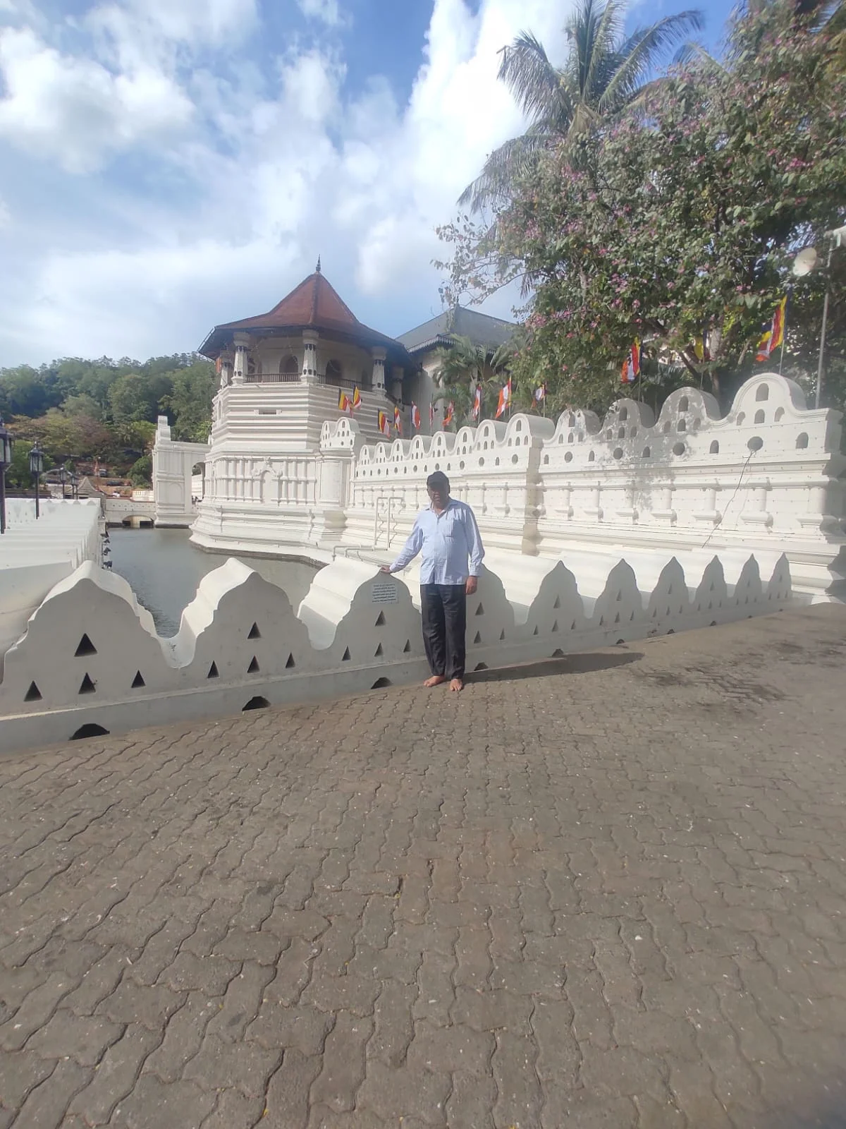Male traveler standing beside the ornate white crenellated moat wall of the Sacred Tooth Relic Temple in Kandy