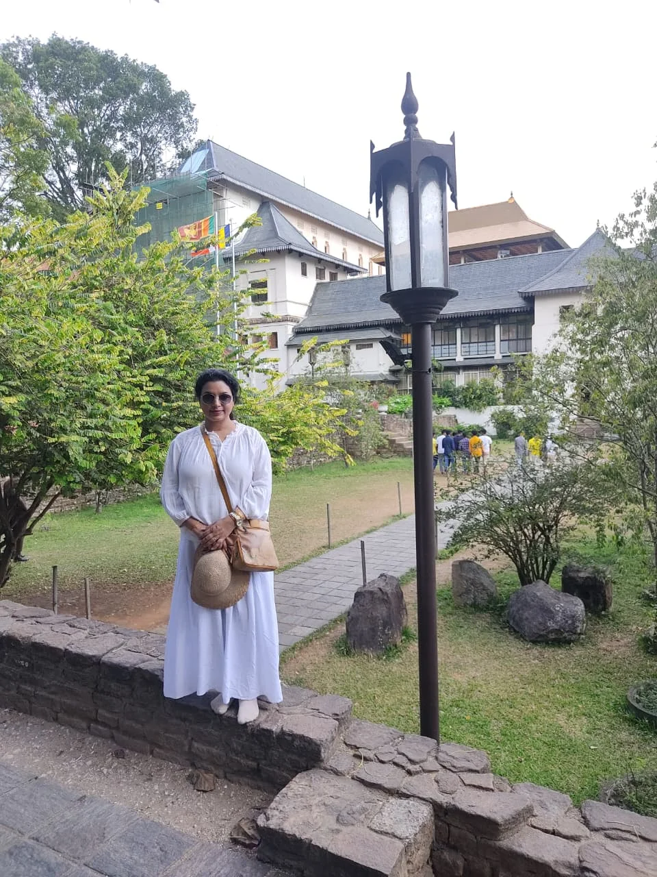 Female traveler in white attire standing on the ancient stone parapet overlooking the sacred temple grounds and heritage pavilions