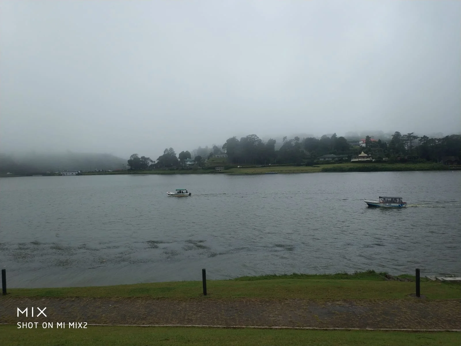 Calm misty expanse of Gregory Lake with small boats gliding over water beneath cloud-covered mountains