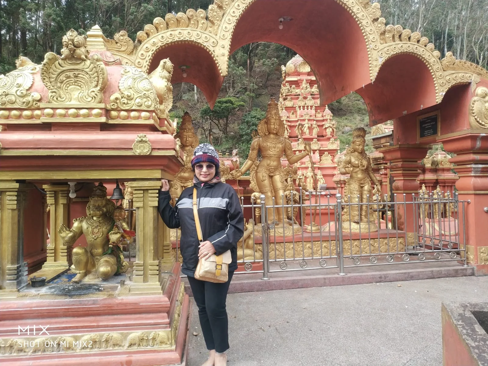 Traveler standing before the ornate golden deities of Lord Rama, Sita Mata, Lakshmana, and kneeling Hanuman at the Seetha Amman Temple in Nuwara Eliya