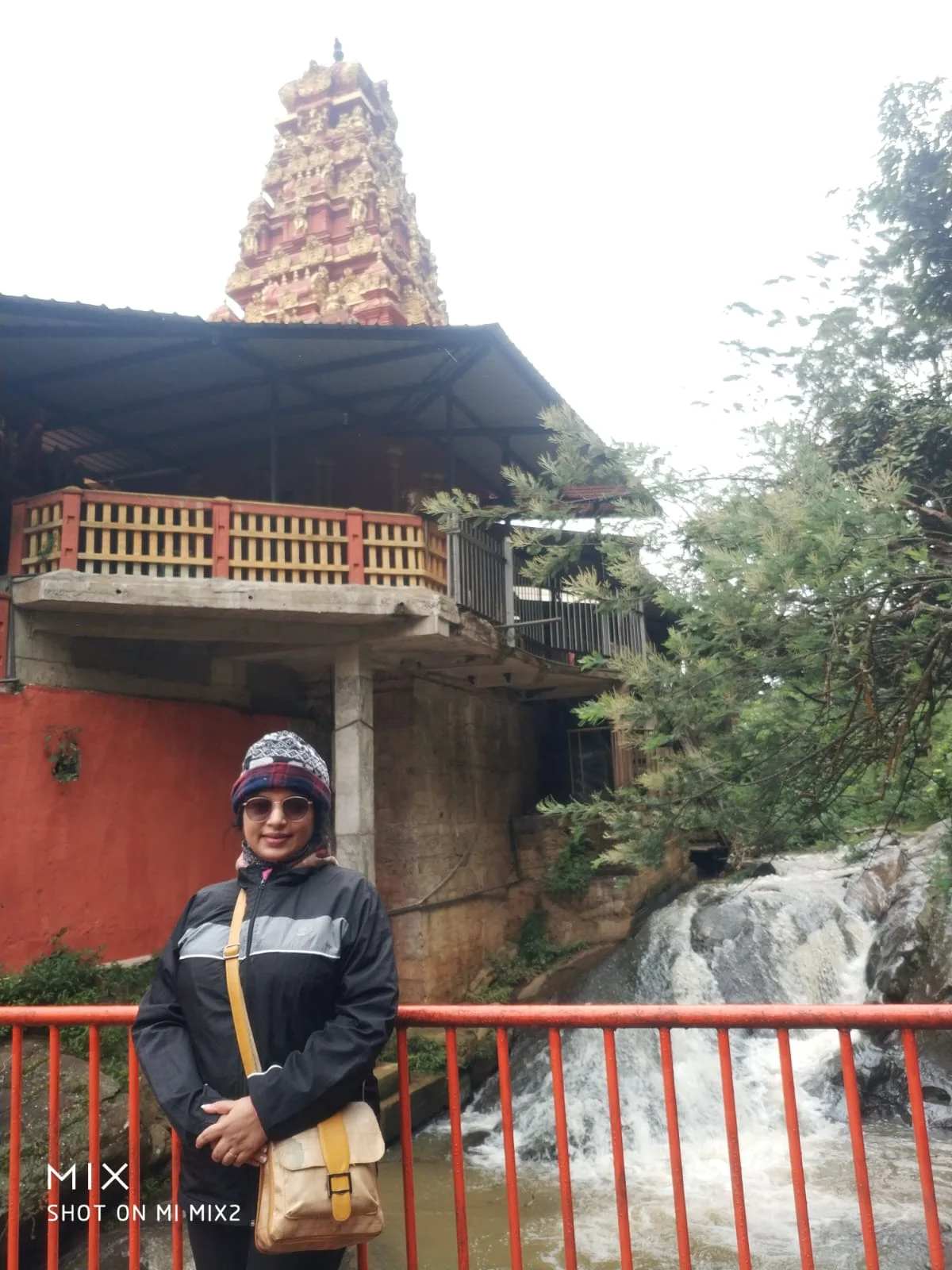 Traveler in warm winter clothing standing on bridge beside the rushing waterfall and sacred mountain stream next to Seetha Amman Temple