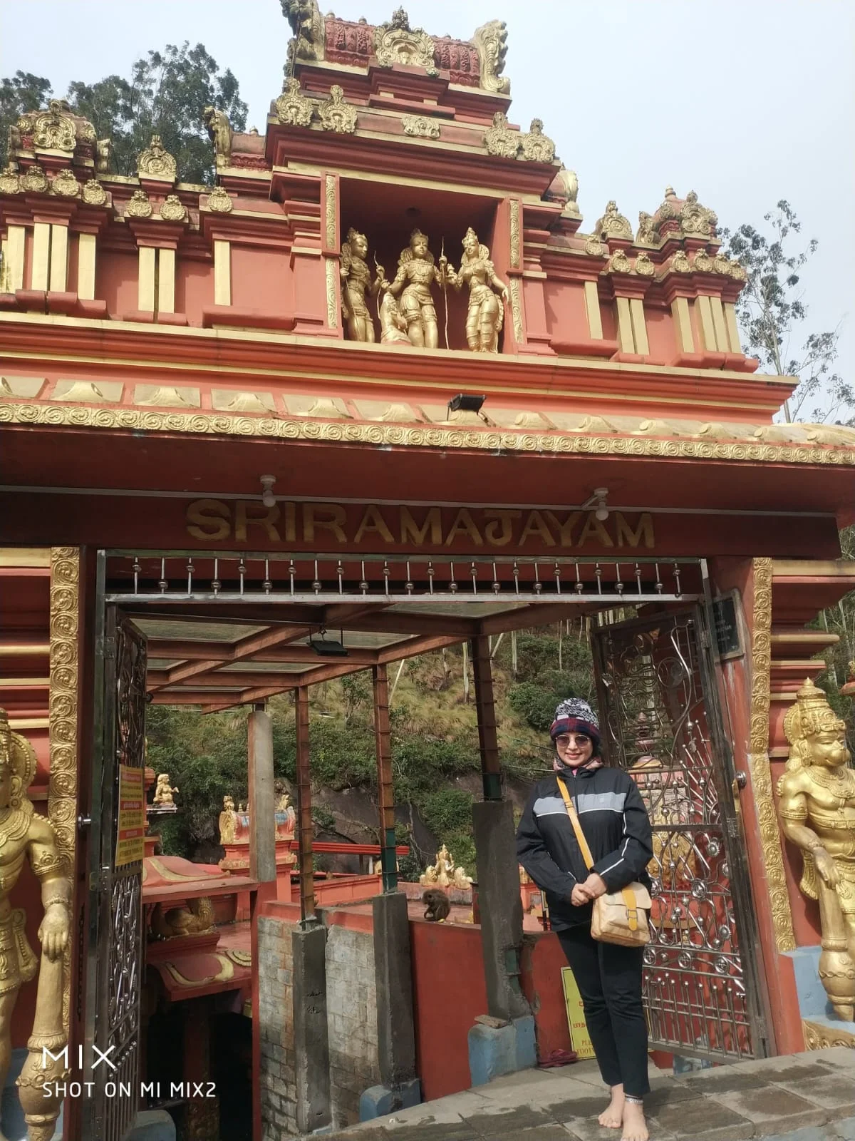 Traveler standing beneath the ornate entrance gateway of Seetha Amman Temple inscribed with SRIRAMAJAYAM and crowned with deities