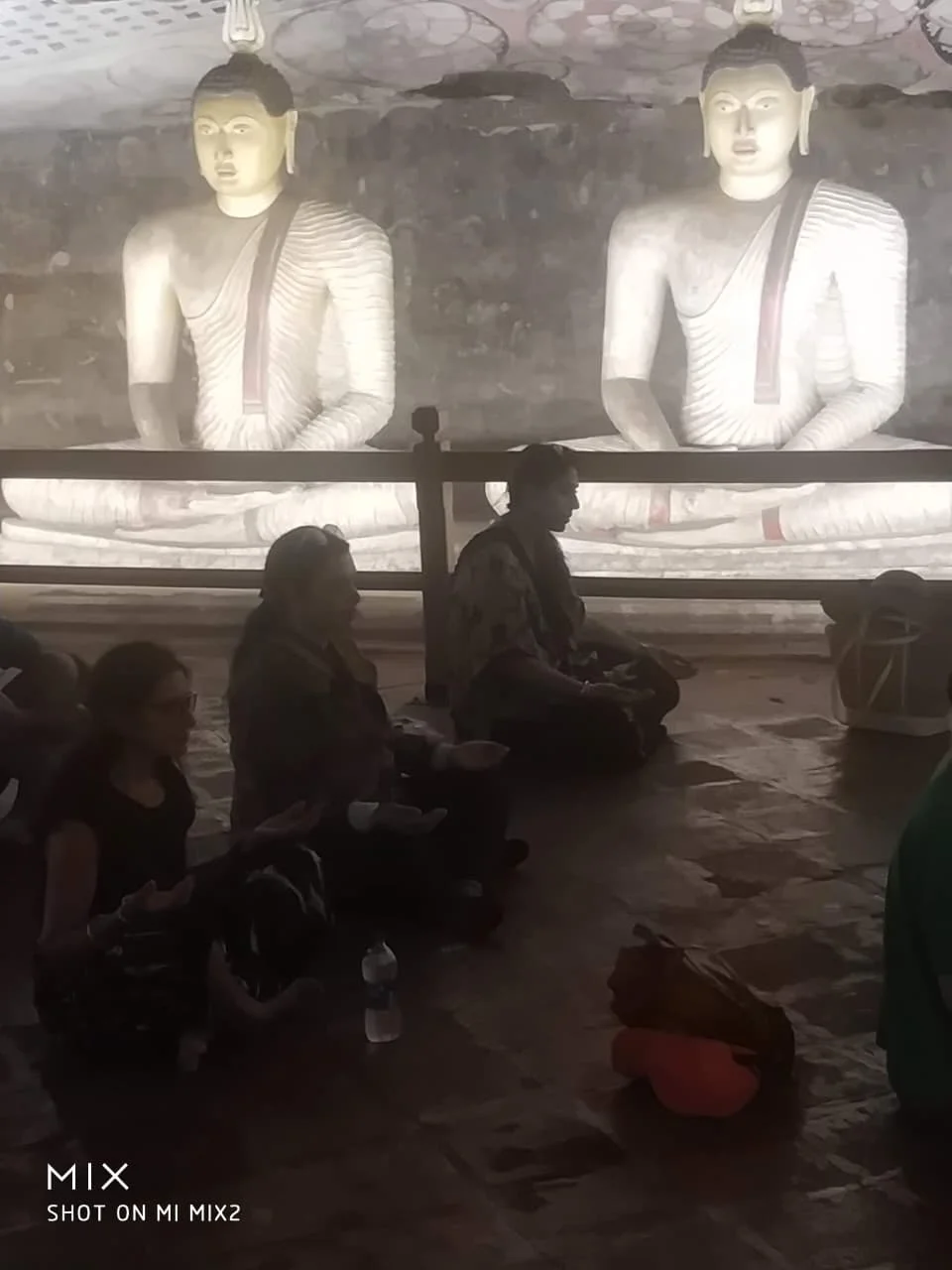 Travelers seated in quiet contemplation before illuminated Buddhas in Dambulla cave