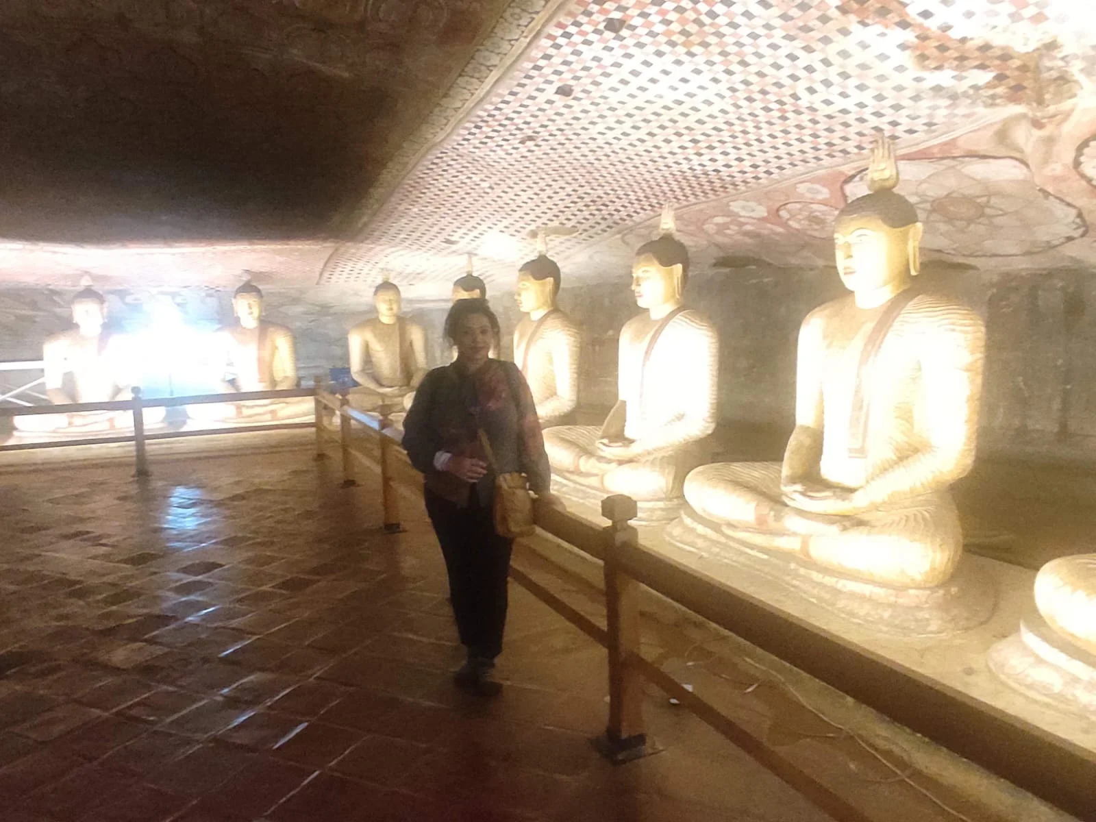 Painted rock ceiling vaults and row of illuminated seated Buddhas in Dambulla cave sanctuary