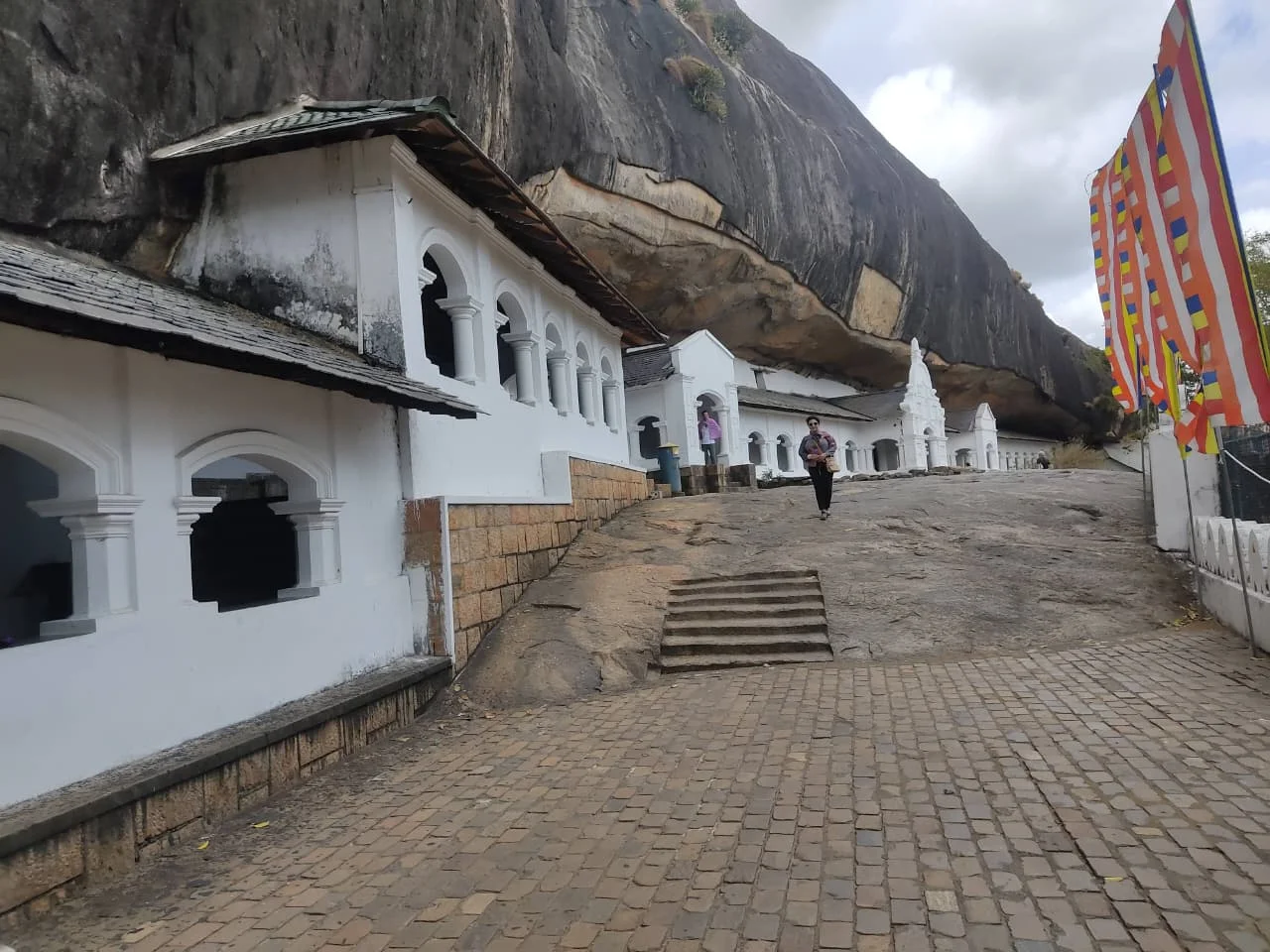 Whitewashed veranda facade nestled beneath the colossal sheer granite overhang of Dambulla