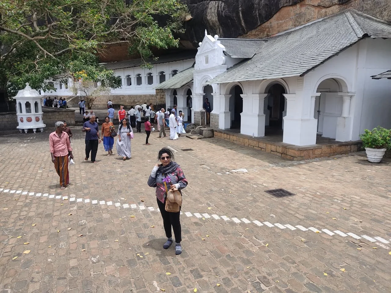 Stone terrace pathway and pilgrims walking beneath the sacred rock of Dambulla