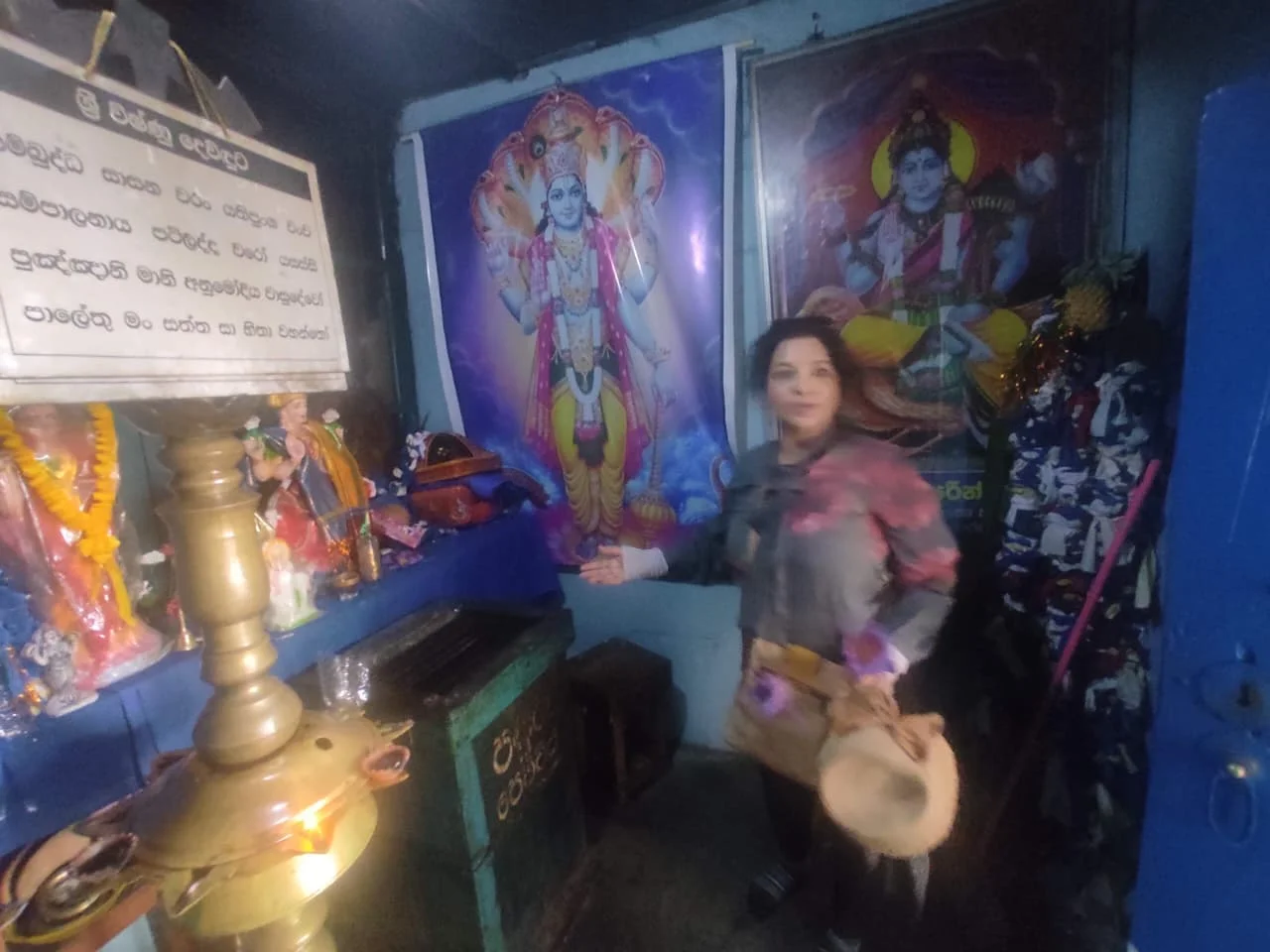Traveler inside the Vishnu Devale shrine at Dambulla Cave Temple with brass lamp and rock mural