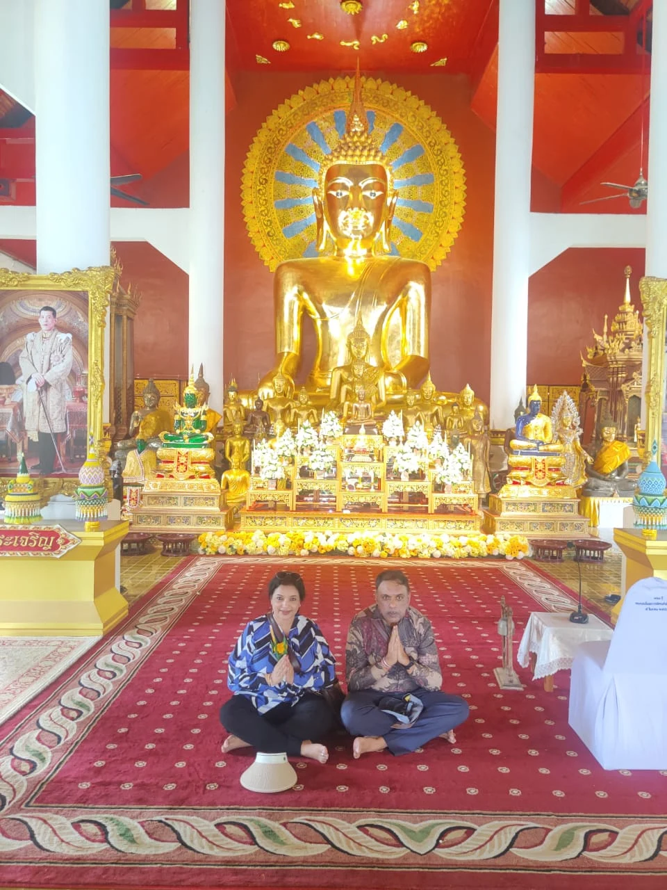 Couple seated in quiet prayer on the red carpet before the colossal golden Buddha inside Viharn Luang