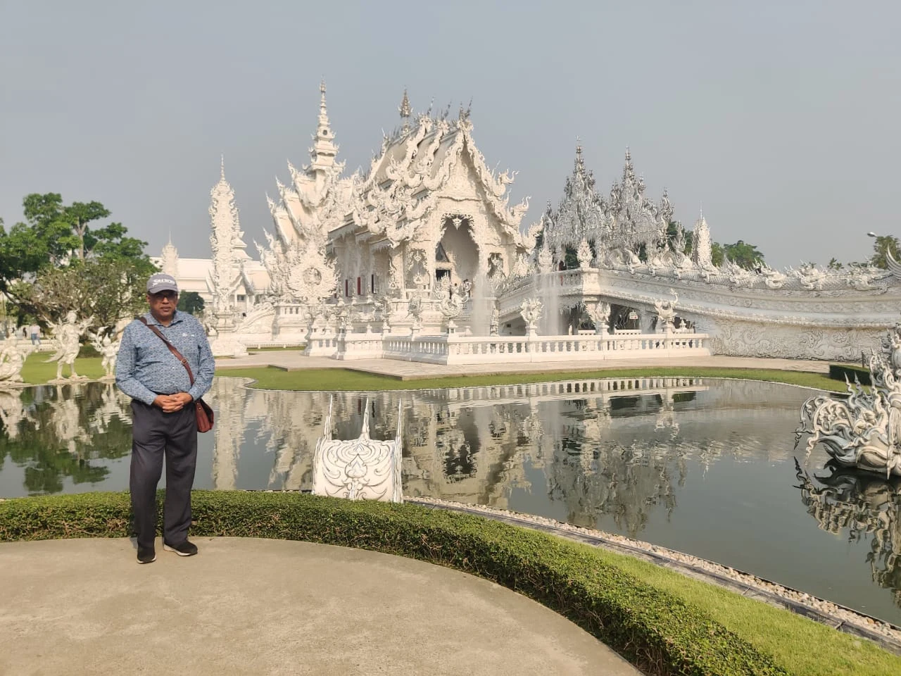 Luminous white spires of Wat Rong Khun reflecting across the sacred pond