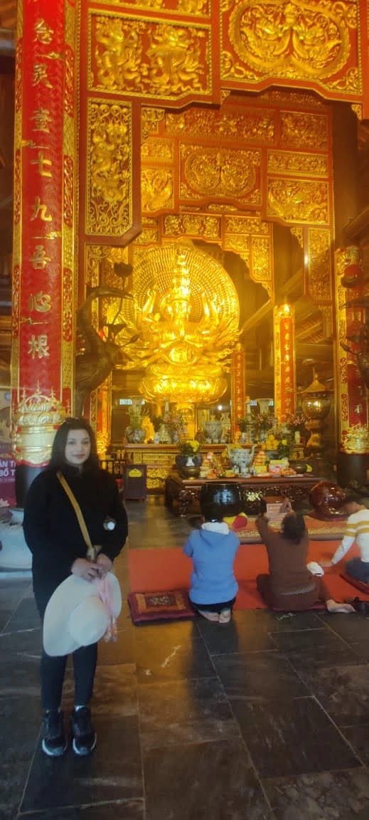 Traveler before the Thousand-Armed Avalokiteshvara Quan Am hall at Bai Dinh Pagoda with devotees in prayer