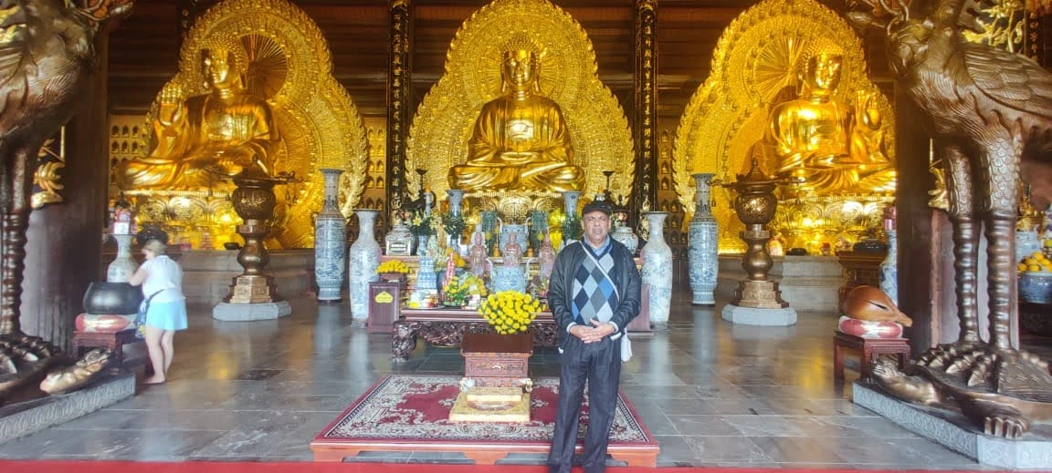 Male traveler standing before the monumental Three Jewels Trikaya Golden Buddhas inside Bai Dinh Pagoda