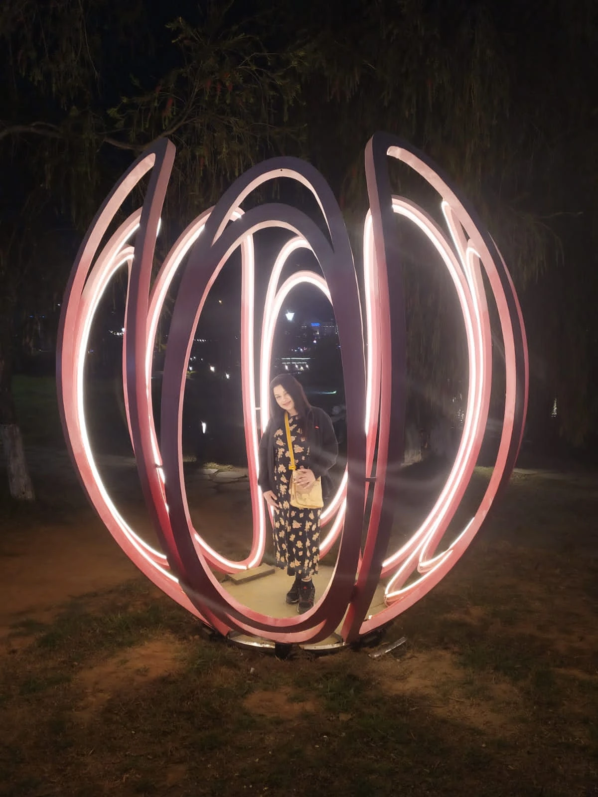 Female traveler standing inside a large illuminated neon lotus flower sculpture at night