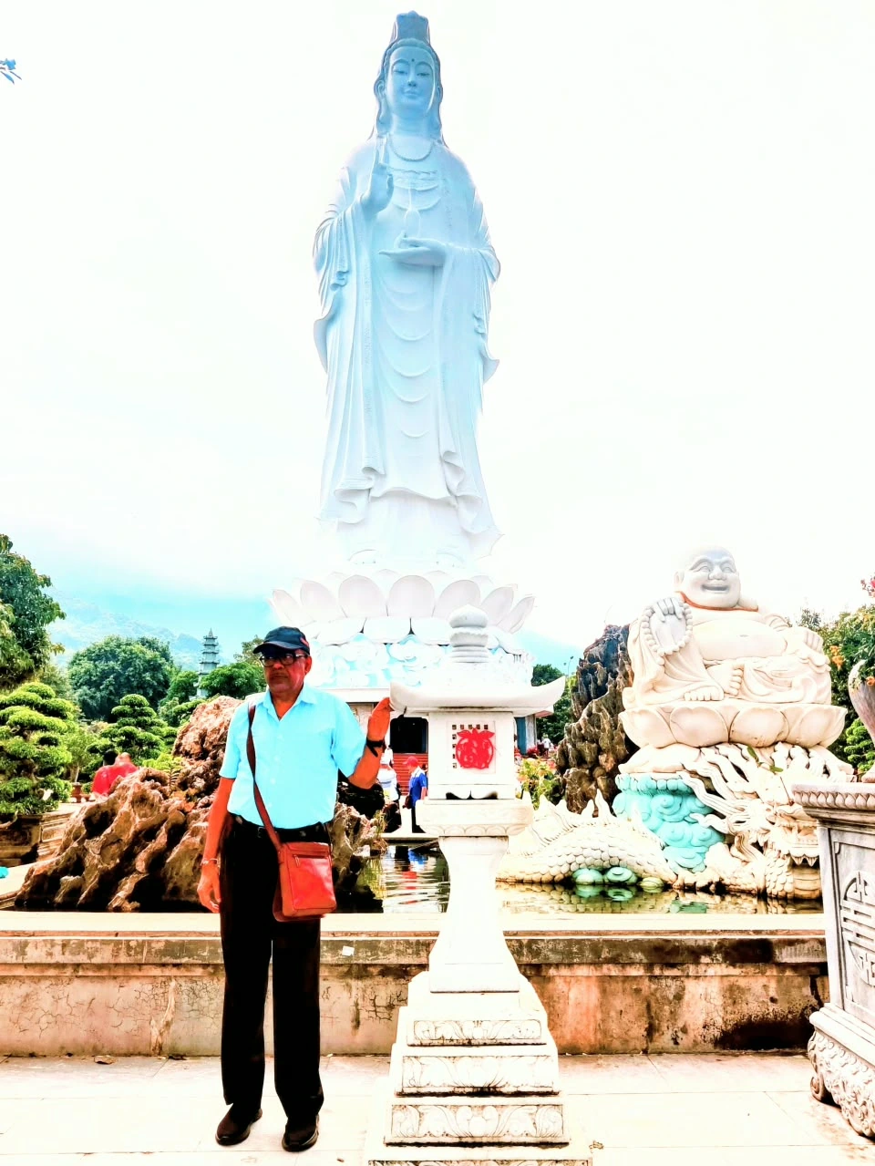 Male traveler standing before the colossal white Lady Buddha Quan Am statue on Son Tra Peninsula in Da Nang