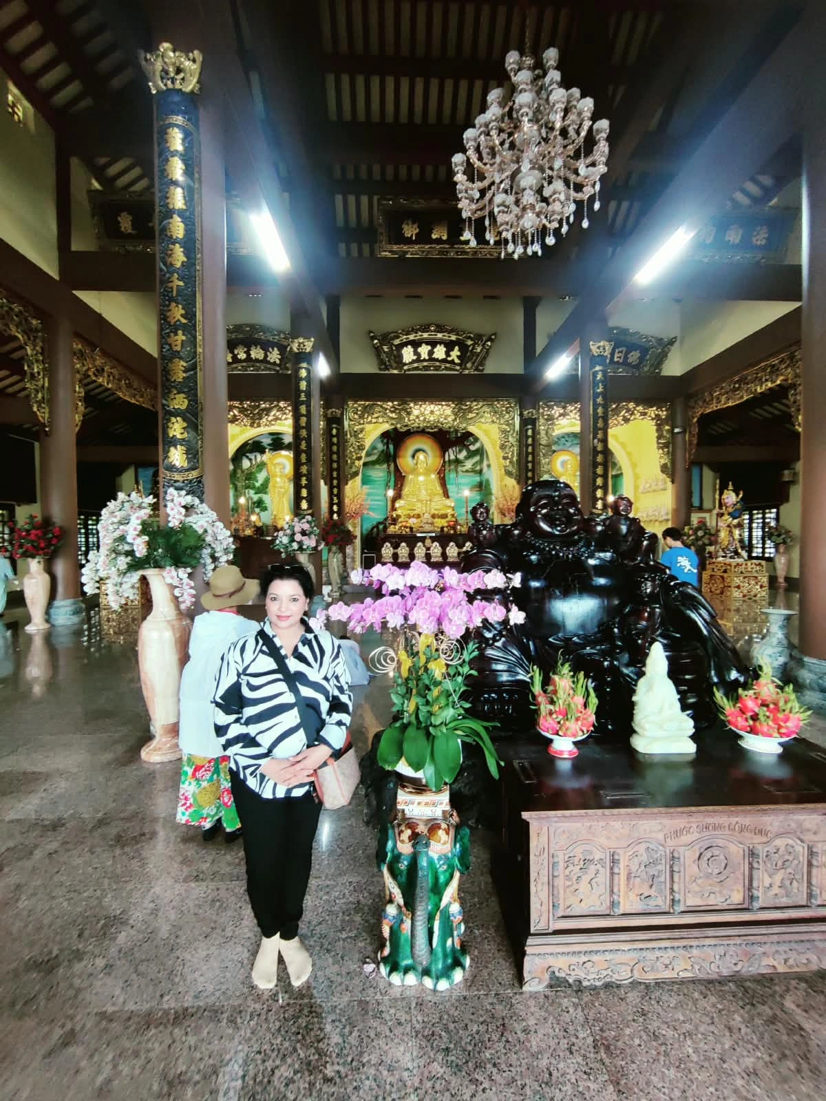 Female traveler inside Linh Ung Pagoda interior hall in front of bronze Maitreya Buddha altar and orchids