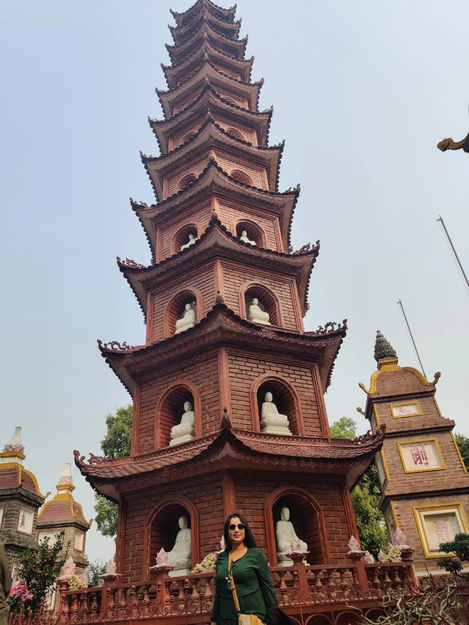 Female traveler standing before the 11-tier red stupa tower Bảo Tháp at Tran Quoc Pagoda with white Buddha statues