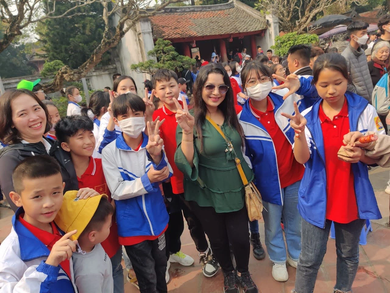 Female traveler surrounded by smiling local Vietnamese school children visiting the historic pagoda