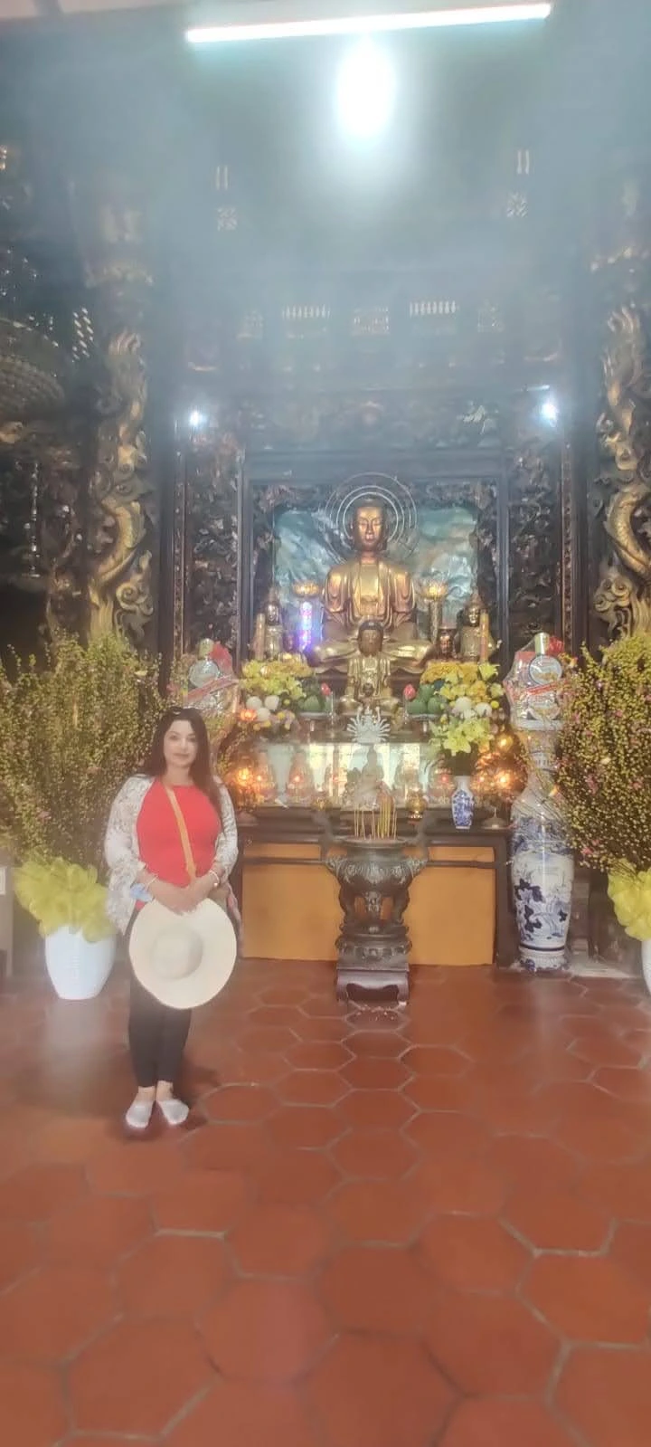 Female traveler before the golden Buddha altar in the incense-filled sanctuary hall of Vinh Trang Pagoda