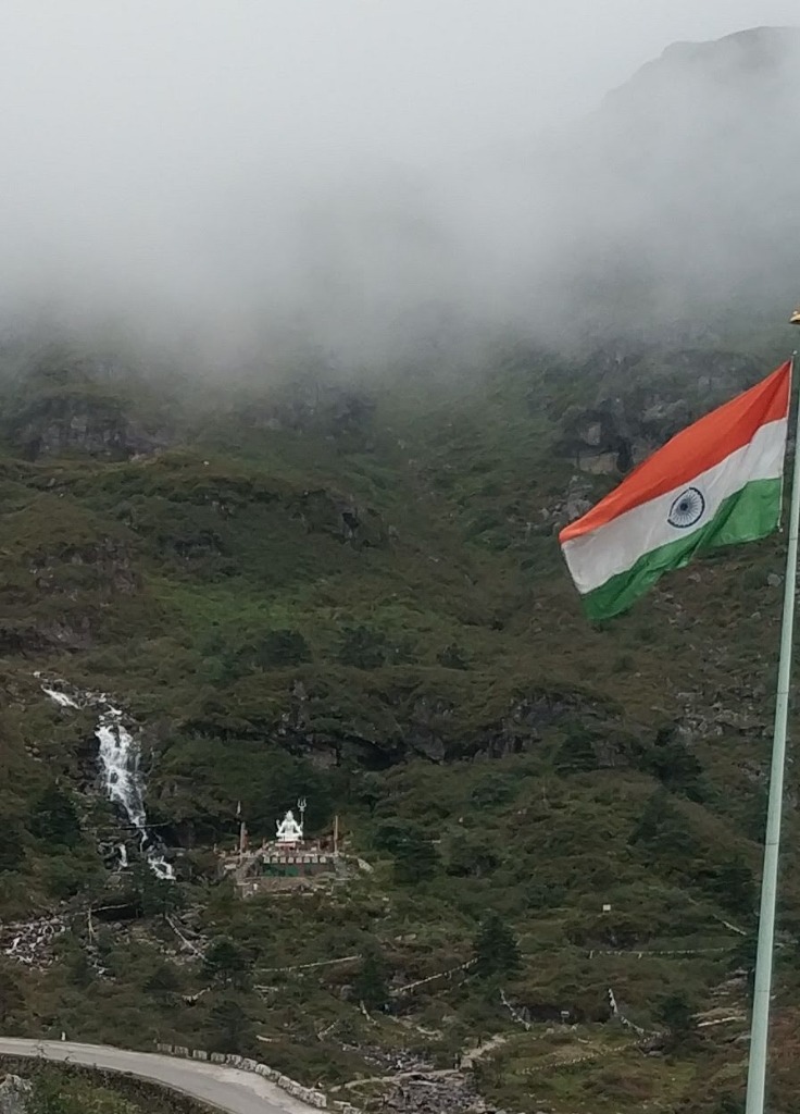 Indian Tricolor Flag fluttering against mountain slopes with Shiva statue at Baba Mandir
