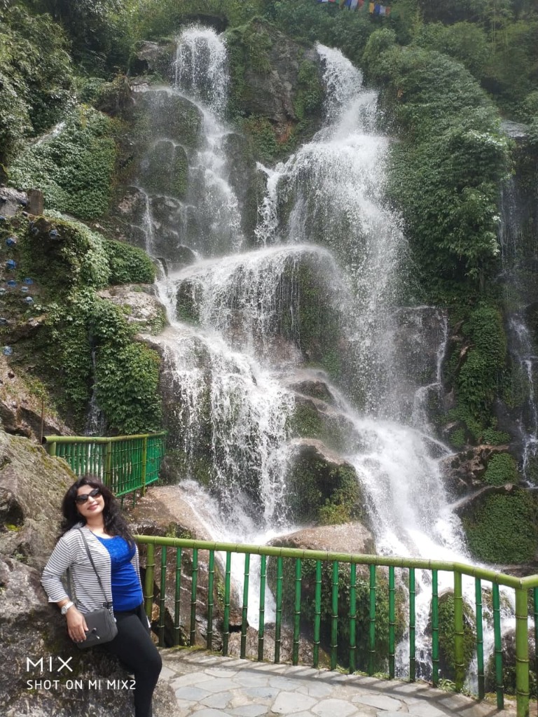 A traveler posing beside the cascading mountain waterfall framed by green bamboo railings in Gangtok, Sikkim