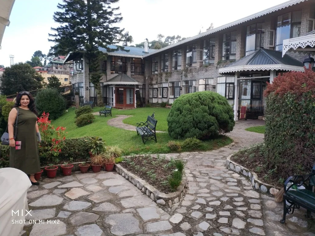 A woman standing in the manicured gardens in front of a grand colonial heritage hotel