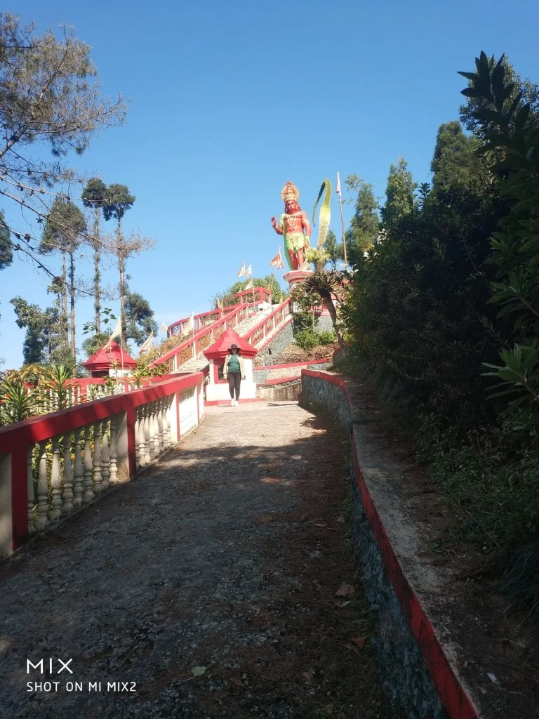 A woman walking up the steps towards a large statue of Lord Hanuman at Hanuman Tok in Kalimpong
