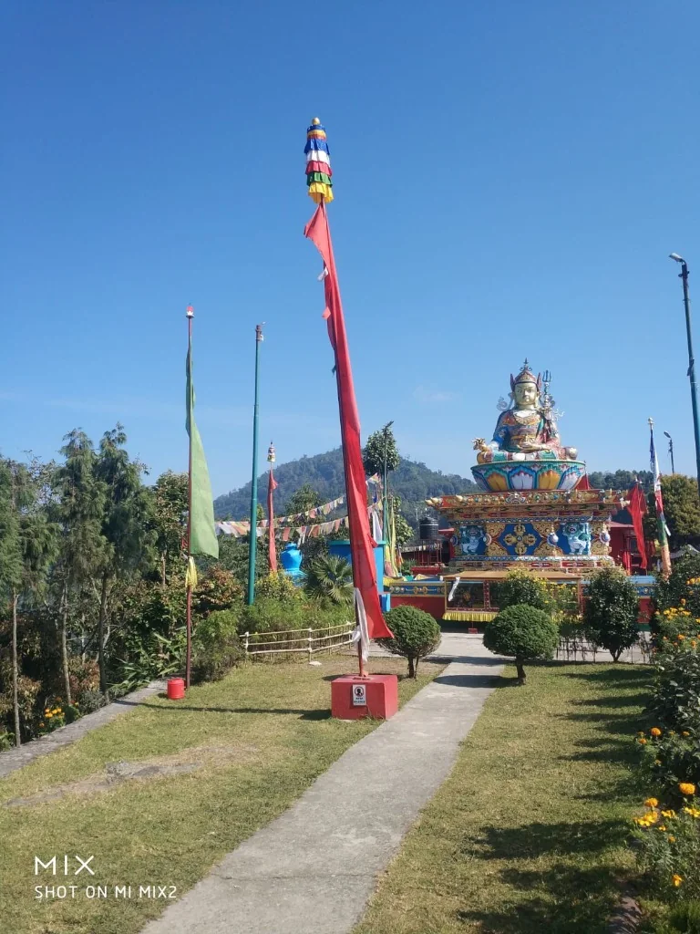 A golden Buddhist statue outdoors on a pedestal with tall prayer flags