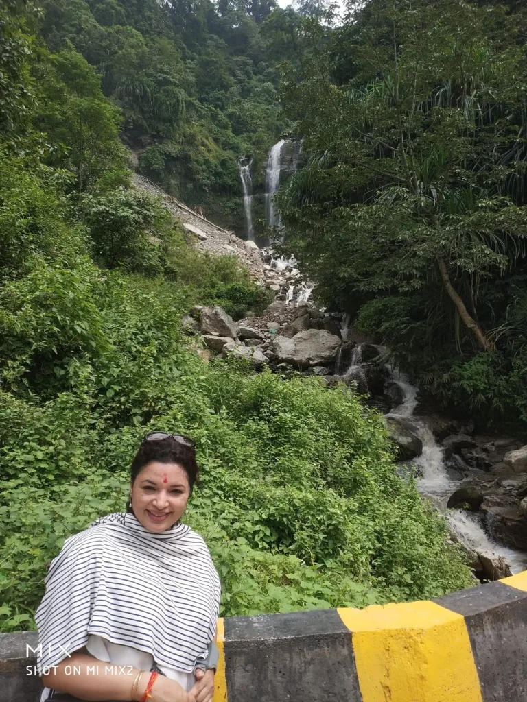 A woman posing in front of a beautiful roadside waterfall in Kalimpong