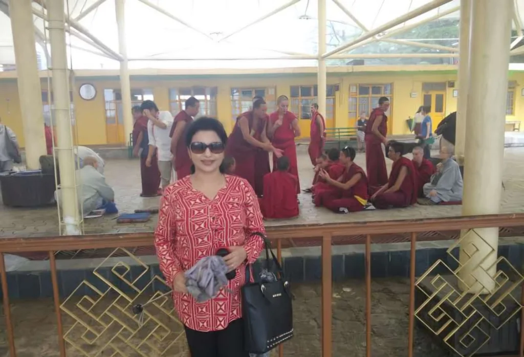 Traveler standing in front of Namgyal Monastery courtyard where monks are gathered in red robes