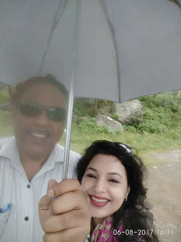 Wanderers smiling under a grey umbrella during rainfall at Neugal Khad
