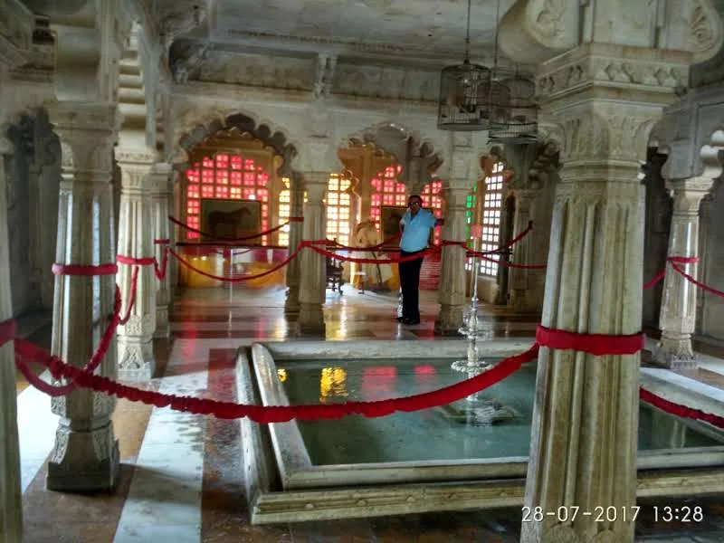 Marble fountain pool with carved pillars and red stained-glass windows inside Badi Mahal at Udaipur City Palace Museum